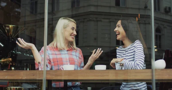 Dos hermosas caucásicas amigable joven mujer charlando alegremente mientras bebe café en la cafetería . — Foto de Stock