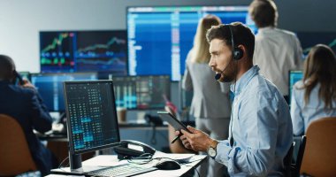 Borsada çalışan profesyonel bir borsacı. Yoğun iş ekibinin arka planında kulaklık ve dijital tablet kullanıyor..