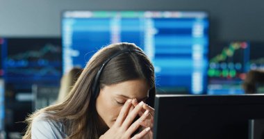 Borsa ofisinde çalışan kadın tüccar veya simsarın portresini birden fazla monitörün arka planında veri, saat numaraları ve grafikleri gösteren bilgisayar kullanarak kapat.