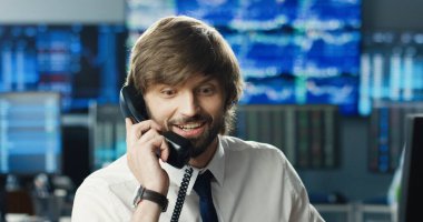 Borsacı ya da finansal analistin portresi, yoğun iş ekibinin arka planındaki monitöre bakarak telefonla konuşuyor..