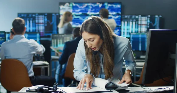 专业的女性经纪人在证券交易所使用耳机在她忙碌的商业团队背景下处理文件 工作中的交易商和经纪人 — 图库照片