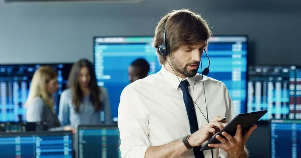 Portrait of trader or brokers working at stock exchange office using headset and digital tablet on background of his business team. Investment Entrepreneur Trading Concept.