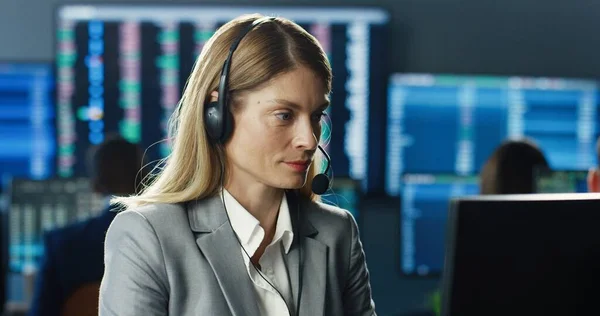利用耳机和计算机在工作站上操作的女性股票交易商的画像 背景是显示数据 发卡号码和图表的多个监视器 商业团队 贸易概念 — 图库照片