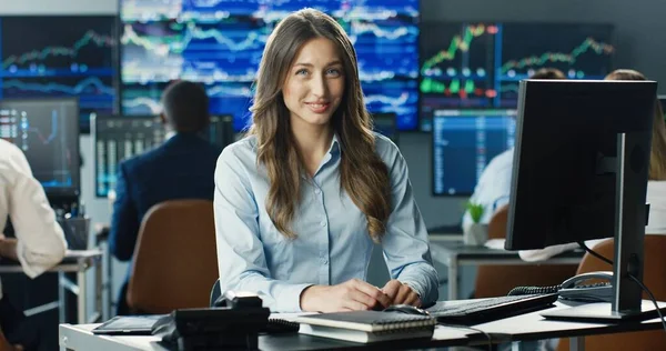 利用计算机描绘女股票交易商在其工作站工作的形象 并在显示数据 打卡号和图表的多个监视器的背景下看着摄像机 — 图库照片