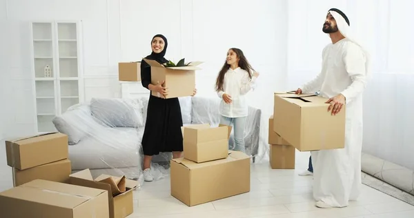 Famiglia araba felice con bambini che entrano in nuova casa e trasportano scatole di cartone. Madre, padre con figli che entrano in casa dopo la riparazione e si guardano intorno con un sorriso. Genitori e figli che si trasferiscono a. — Foto Stock