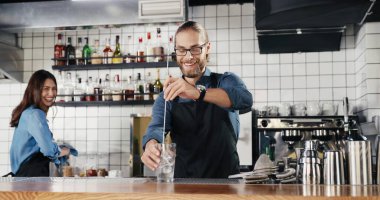 Beyaz, yakışıklı ve neşeli bir barmen. Buzlu içki hazırlıyor ve bayan meslektaşlarına gülümsüyor. Garson ve garson konuşuyor. Barmen, barda buzla kokteyl yapıyor..