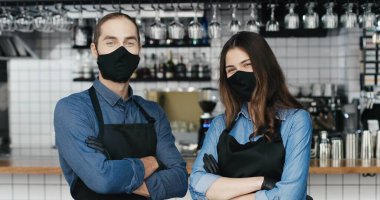 Maskeli ve eldivenli genç beyaz barmenlerin birbirlerine bakıp kameraya mutlu bir şekilde gülümsedikleri portre. Kafedeki mutlu garson ve garson. Neşeli erkek ve kadın, işte Noel..