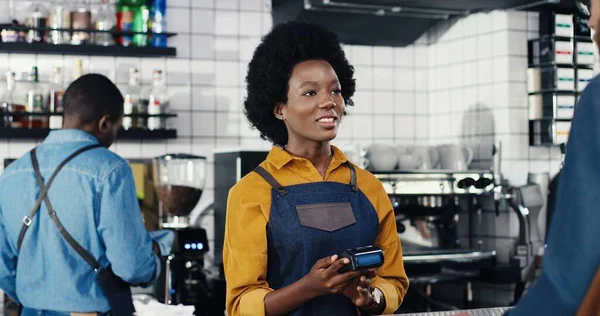 Multietnisk bartender kvinna och klient man. Vit man betalar med betalkort, kreditkort. Blandraser. Godkänd betalning vid disken. Betala för dryck eller mat på caféet. Afrikansk amerikansk servitris. — Stockfoto