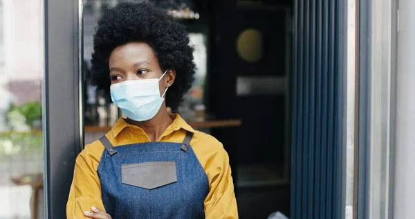 Garçonete menina bonita afro-americana abrindo porta do café e saindo na rua para respirar de ar fresco. Feche-se de barrista fêmea bonita que vai fora. Reabrir conceito durante a pandemia . — Fotografia de Stock