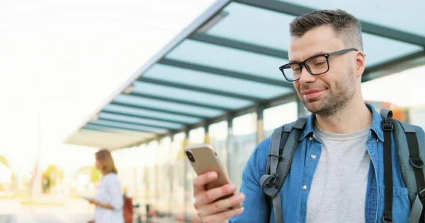 Gözlüklü, sırt çantalı, otobüs durağında duran ve cep telefonunu dinleyen beyaz tenli yakışıklı bir genç. Gözlüklü bir erkek tren istasyonunda cep telefonundan mesaj yolluyor.. — Stok fotoğraf