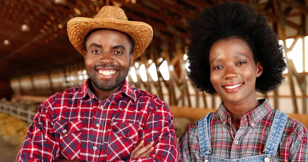 Πορτρέτο της ευτυχούς Αφρικής Αμερικής νεαρό ζευγάρι των αγροτών στέκεται μαζί και διασχίζουν τα χέρια, ενώ χαμογελώντας στην κάμερα στο αγρόκτημα πρόβατα υπόστεγο. Γυναίκα και άντρας σε στάβλο. Άνδρες και γυναίκες χαρούμενοι εργαζόμενοι. — Φωτογραφία Αρχείου