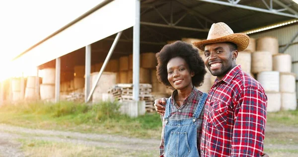 Portret van Afro-Amerikaanse jonge vrolijke gelukkige paar boeren wandelen in knuffels buiten op de boerderij en glimlachen naar de camera. Een landelijke levensstijl. Dorpsconcept. Gelukkige man en vrouw knuffelen. Omhels. — Stockfoto