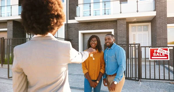 Posteriore di immobili che vendono casa a coppia afro-americana felice e consegna chiavi. All'aperto. Gioioso uomo e donna sposato che si abbracciano e comprano casa alla periferia. Sto per abitare in periferia. vista posteriore. — Foto Stock
