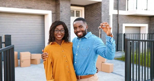 Porträtt av glad ung afroamerikansk man och kvinna ler mot kameran och visar nyckeln till ett nytt hem. Utanför. Köpa fastigheter. Vi går in i konceptet. Oklar. Glada par bosätter sig i. — Stockfoto
