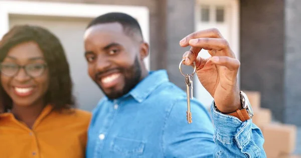 Fechar feliz jovem afro-americano homem e mulher sorrindo para a câmera e demonstrando a chave da nova casa. Ao ar livre. A comprar imóveis. Movendo-se em conceito. Retrato. Desfocado. Casal alegre se estabelecendo em. — Fotografia de Stock