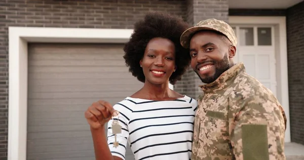 Portrét mladého afroamerického vojáka, jak stojí doma v náručí, usmívá se a ukazuje klíč ke kameře. Muž v uniformě, žena se stěhuje do nového domu. Nemovitost — Stock fotografie