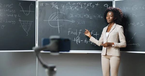 Smartphone opname video virtuele les op webcam op school. Online studeren. Afro-Amerikaanse vrouw docent wiskunde of natuurkunde formules op schoolbord. Opsluitingsconcept. Pandemisch onderzoek. — Stockfoto