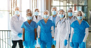Profesyonel erkek ve kadın doktorlardan oluşan melez bir ekip hastanede. Kapalı alanda. Tıbbi maskeli uluslararası bir sağlık ekibi. Klinikte önlüklü ve üniformalı çok ırklı doktorlar var..