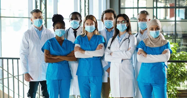 남녀 의사로 구성 된 혼혈 인종들이 병원에서 촬영하고 악수하기 위해 포즈를 취하고 있습니다. 국제 의료진들이 의료용 마스크를 쓰고 있습니다. 진료소에서 여러 민족의 의사와 간호사를 보호하다 — 스톡 사진