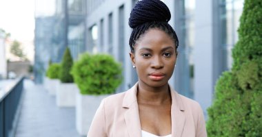 Genç Afro-Amerikan güzel bir kadının portresi. Ciddi bir şekilde dışarıda kameraya bakıyor. İş merkezinin yakınındaki caddede kendine güvenen çekici bir iş kadınına yaklaş. Dolly vurdu. Yakınlaştırılıyor.