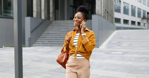 아프리카계 미국인아름다운 미소짓는 여성이 핸드폰으로 말하고 밖을 걷고 있었습니다. 휴대폰으로 말하고 걷는 쾌활 한 여성. 전화 통화. — 스톡 사진