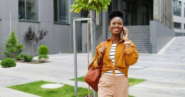 Afrikansk amerikan vacker glad leende kvinna talar på mobiltelefon och går utanför. Glada kvinna talar på mobiltelefon och promenader. Telefonsamtal. — Stockfoto