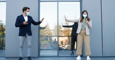 Beyaz erkek ve kadın iş stili ve tıbbi maskeli sosyal mesafede duruyor ve akıllı telefonlardan mesajlar yolluyorlar. İş adamı ve iş kadını dışarıda cep telefonu kullanıyor. Karantina.