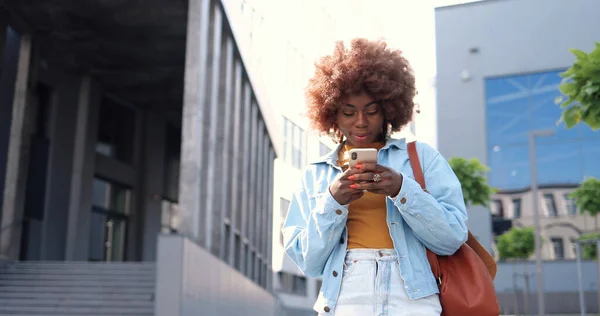곱슬머리의 아프리카계 미국인젊은 여성이 스마트폰으로 두드리거나 스크롤을 시가지에 있습니다 아름다운 — 스톡 사진