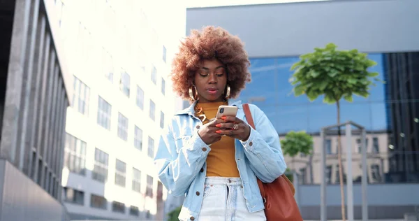 아프리카계 미국인젊은 곱슬머리의 스마트폰으로 두드리거나 스크롤을 시가지에 — 스톡 사진