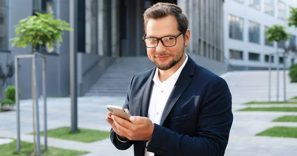 Caucasian attractive young stylish man tapping or scrolling on tablet device in town at street. Handsome male texting message and using gadget computer.