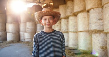 Kafkasyalı, şapkalı, saman yığınlarıyla kulübede duran ve kameraya gülümseyen hoş bir çocuğun portresi. Ahırda küçük bir çocuk. Kırsal kesimde yaz. Köyde çocukluk..