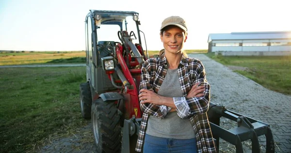 Portret młodej, białej, pięknej kobiety w kapeluszu, stojącej na polu w dużym ciągniku i uśmiechniętej do kamery. Ładna pracownica rolnictwa na świeżym powietrzu. Koncepcja rolnictwa. — Zdjęcie stockowe
