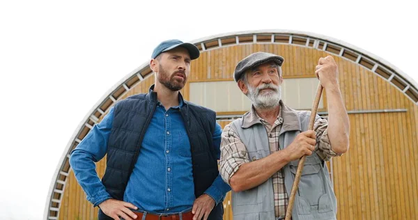 Kaukasische jongeman buiten met oude gepensioneerde vader op de boerderij en praten, vragen om advies. Mannen boeren spreken en discussiëren over landbouwwerk. Het platteland. Zoon en senior vader. — Stockfoto