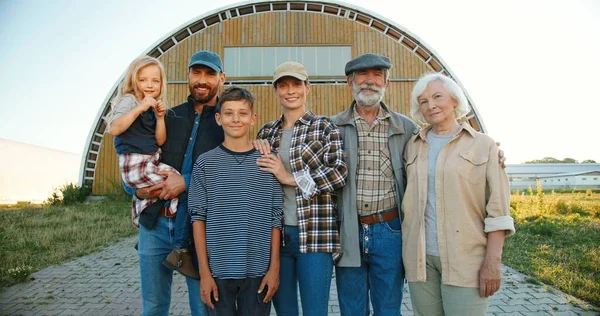 Portret fericit Caucazian familie de trei generații în aer liber în magazie fermă și zâmbind camerei. Părinți vechi cu copii și nepoți în mediul rural. Fermieri. Summer. Stilul de viață — Fotografie, imagine de stoc