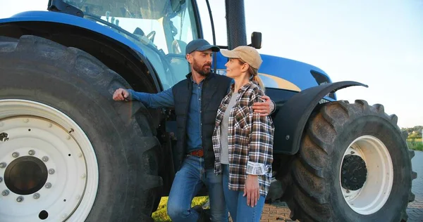 Portrait of Caucasian happy couple of married farmers standing in hugs at tractor, looking at each other and smiling to camera. Outdoor. Man hugging woman in field. Farming concept. Wife and husband. — Stock Photo, Image