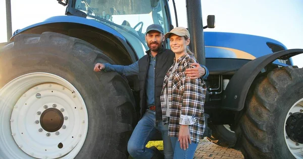 Portrait of Caucasian happy couple of married farmers standing in hugs at tractor, looking at each other and smiling to camera. Outdoor. Man hugging woman in field. Farming concept. Wife and husband. — Stock Photo, Image
