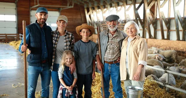 Portrait of happy Caucasian family of three generations standing in shed with livestock and smiling. Old parents with children and grandchildren in stable. farmers at farm. Indoor. Sheep on background — Stock Photo, Image