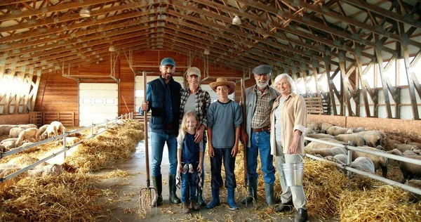 Portrait de heureuse famille caucasienne de trois générations debout dans hangar avec du bétail et souriant. Vieux parents avec enfants et petits-enfants dans l'écurie. Des agriculteurs avec des enfants à la ferme. Zoom arrière. — Photo