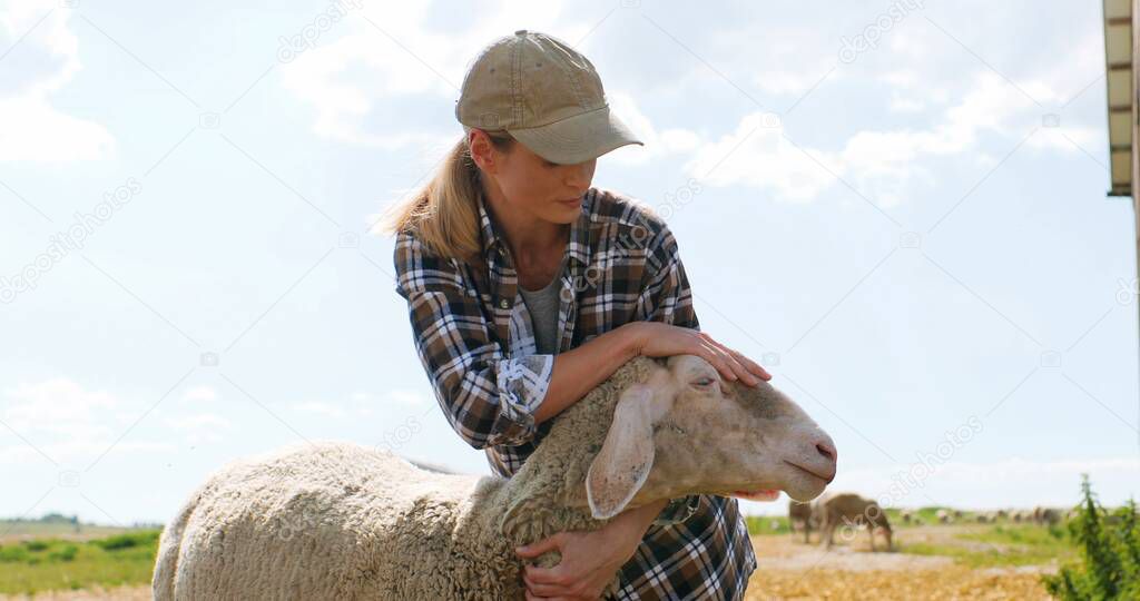 Caucasian pretty young woman shepherd holding sheep and petting it outdoors. Beautiful female farmer caressing and stroking animal. Livestock farming concept. Outdoors.