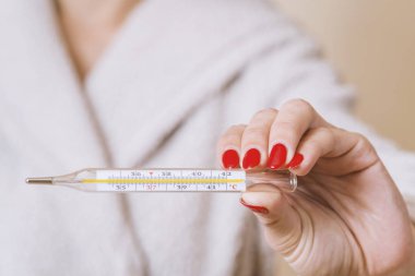 Ellerinde termometre tutan kadın gripten acı çekerken vücut ısısını ölçüyor..
