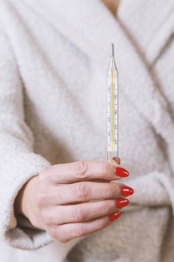 Ellerinde termometre tutan kadın gripten acı çekerken vücut ısısını ölçüyor..