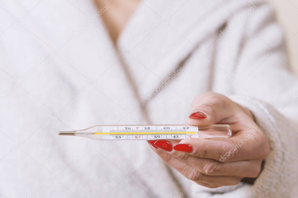 woman holding thermometer in hands, measuring body temperature while suffering from influenza.