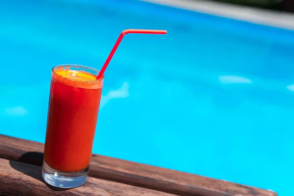 juice in a glass on the wooden table by the pool.