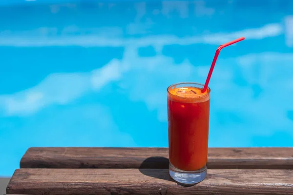 juice in a glass on the wooden table by the pool.