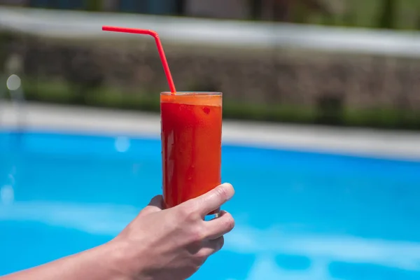 juice in a glass on the wooden table by the pool.