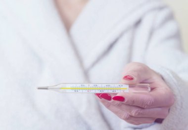 Ellerinde termometre tutan kadın gripten acı çekerken vücut ısısını ölçüyor..