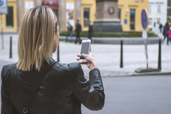 Kadın turist sokakta cep kamerasıyla fotoğraf çekiyor.