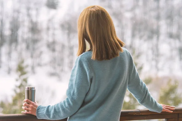 Woman in the background of a winter forest in a thermos bottle in hands