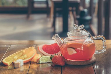 Cam çaydanlıkta meyveli kırmızı çay ve ahşap arka planda fincan.