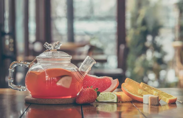 Fruit red tea in a glass kettle and cup on the wooden background